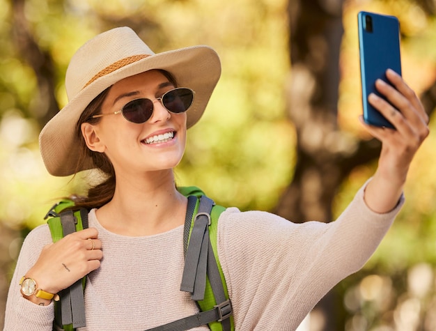 Selfie z telefonem natury i kobieta wędrująca w okularach przeciwsłonecznych w kapeluszu i uśmiechnięta przygoda w lesie lub lesie latem Swoboda spokój i spacer po drzewach, aby zrelaksować się i cieszyć się weekendem