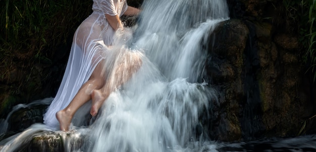 Seminude młoda kobieta w białej sukni cieszy się świeżością i chłodem w strumieniach wody wodospadu
