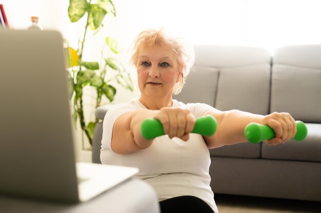 Senior kobieta ćwiczenia za pomocą instrukcji online laptopa w domu opieki zdrowotnej.