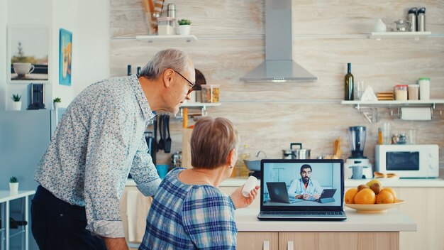 Senior kobieta podczas wideokonferencji z lekarzem pokazując butelkę tabletek. Konsultacje zdrowotne online dla osób starszych porady dotyczące chorób narkotykowych, lekarz telemedycyna kamera internetowa. Stażysta opieki medycznej