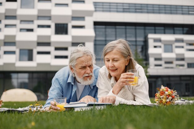 Senior para leżąc na kocu na pikniku latem i czytając książkę