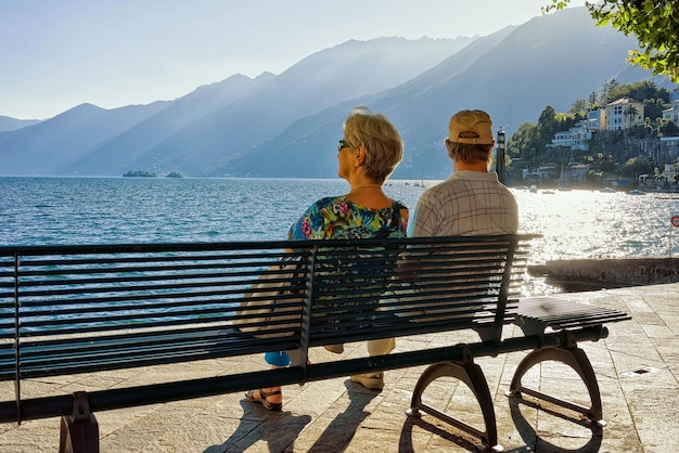 Senior para siedzi na ławce na nabrzeżu luksusowego kurortu Ascona nad jeziorem Maggiore, kanton Ticino w Szwajcarii.