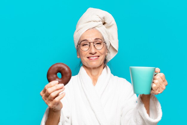 Senior Pretty Woman Po Prysznicem I Nosząc Szlafrok I Jedząc śniadanie Z Kawą I Pączkiem