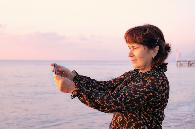 Seniorka fotografuje morski krajobraz na plaży w świetle wschodzącego słońca