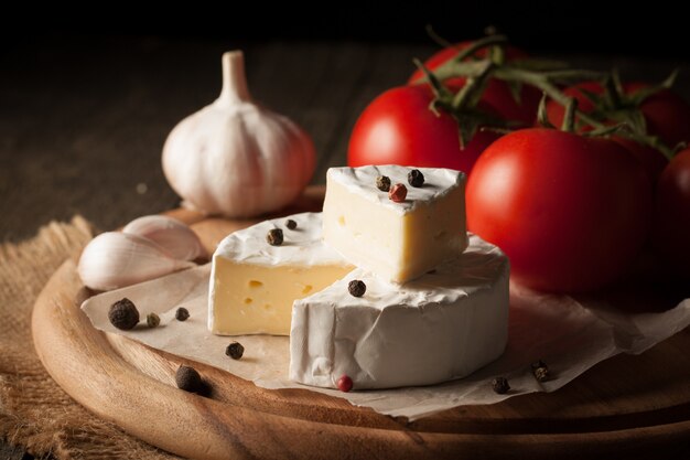 Ser Camembert i Brie na drewnianym tle z pomidorami, sałatą i czosnkiem. Włoskie jedzenie. Nabiał.