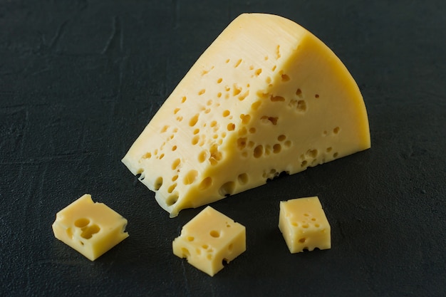 Ser Radamer na czarnym betonowym tle. trójkątny kawałek szwajcarskiego sera z żółtego mleka krowiego z dziurami .