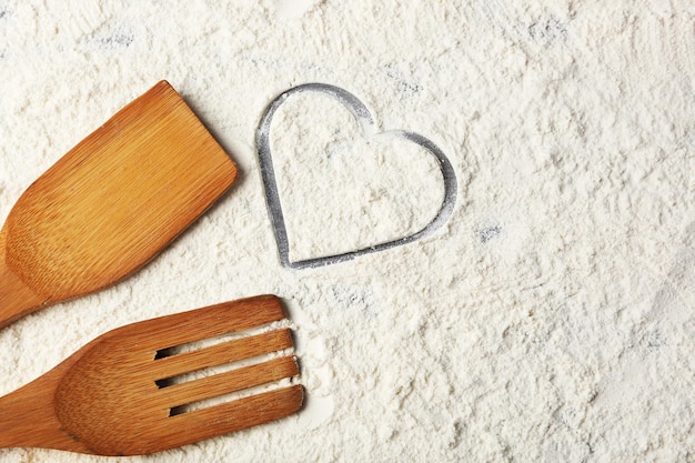Serce z mąki i drewniane naczynia kuchenne n na szarym tle