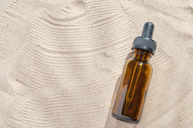 serum do twarzy w szklanej butelce z pipetą na naturalnym tle z piaskiem. makieta piękna