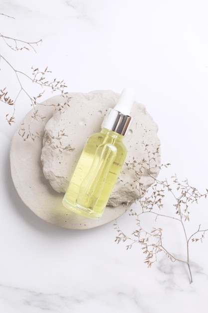 Zdjęcie serum kosmetyczne w szklanej butelce na kamiennym podium markowe projektowanie opakowań produktów kosmetycznych marmurowe tło z gałązką kwiatową