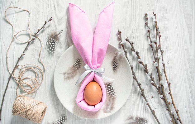 Serwetka w kształcie króliczka wielkanocnego z jajkiem w środku z dekoracją wielkanocną na jasnym tle.