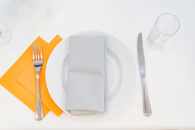 Serwetki stołowe z białym talerzem, widelec z nożem i pustą szklanką na stole