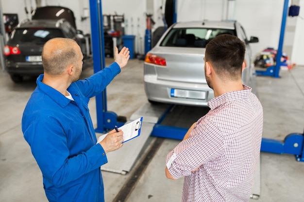 serwis samochodowy, naprawa, konserwacja i koncepcja ludzi - mechanik ze schowkiem rozmawia z mężczyzną lub właścicielem w sklepie samochodowym