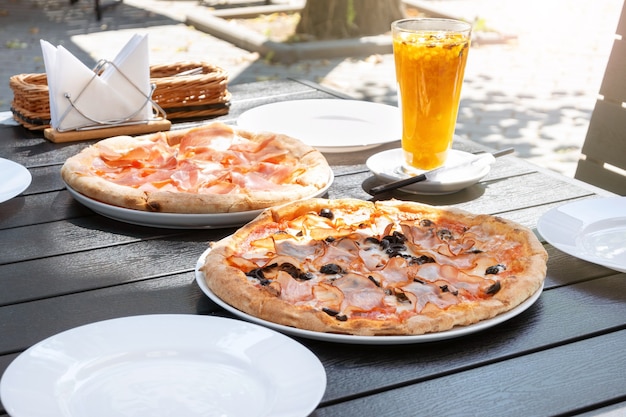 Serwowanie pizzy z szynką prosciutto w ulicznej restauracji. Włoskie jedzenie i herbata z rokitnika na lunch w kawiarni na świeżym powietrzu w słoneczny dzień