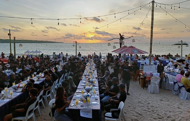 Setki ludzi jedzą, ciesząc się zachodem słońca na plaży Jimbaran.