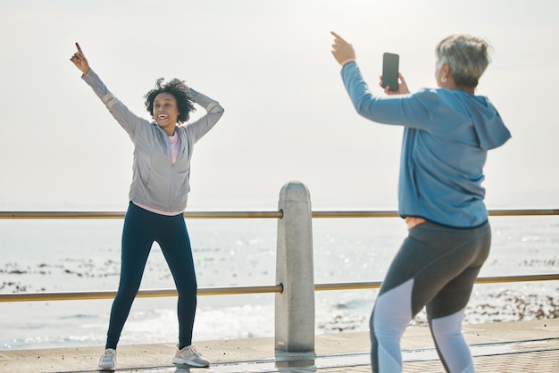 Zdjęcie sfotografuj starszą kobietę i przyjaciół fitness z postem w mediach społecznościowych, czując się głupio nad morzem ćwiczenia treningowe i trening z dojrzałymi ludźmi oraz zdjęcie do zdjęcia profilowego ze wskazaniem nad oceanem