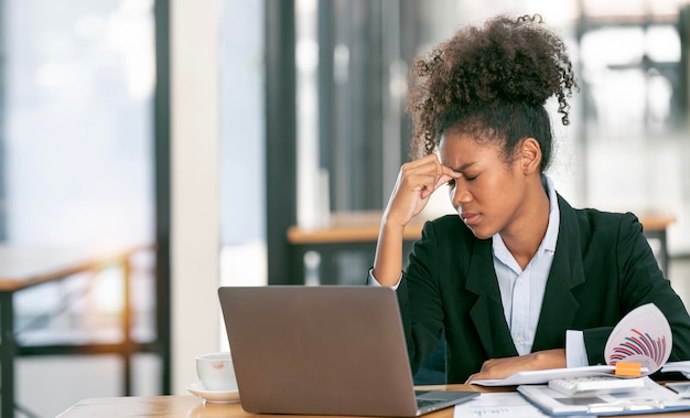 Sfrustrowana młoda Afroamerykanka trzymająca oczy zamknięte i masująca nos po pracy na laptopie przez długi czas w biurze