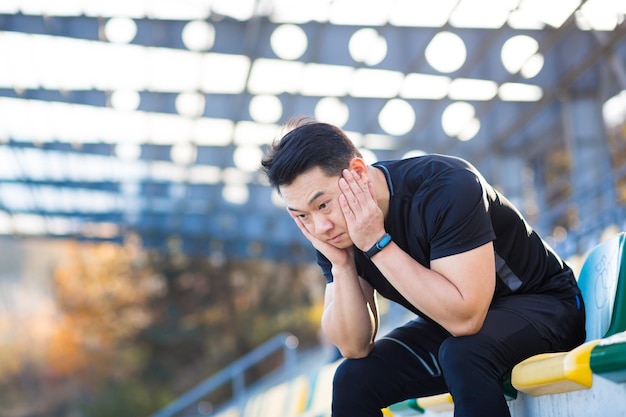 Sfrustrowany azjatycki sportowiec pogrążony w depresji, niezadowolony z wyników swojego treningu w rozpaczy po bieganiu w spoczynku w pozycji siedzącej