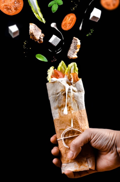 Shawarma pita z kurczakiem w dłoni ze składnikami latającymi w powietrzu