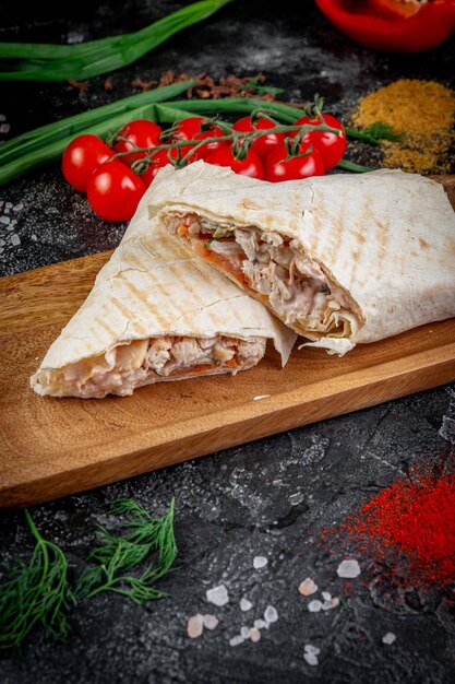 Zdjęcie shawarma z warzywami na drewnianej desce z sosem pita na ciemnym kamiennym stole ozdobionym pomidorkami koktajlowymi usługa dostawy do restauracji fast food