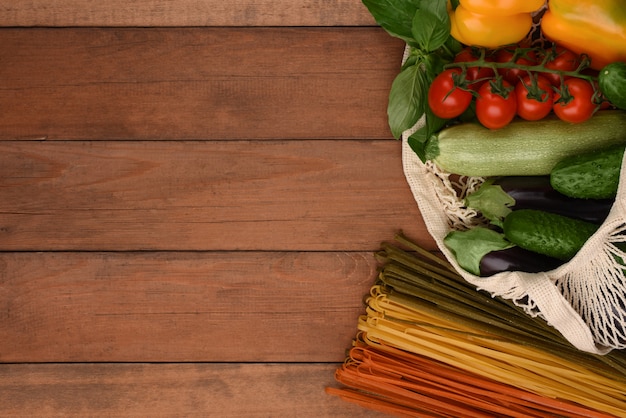 Siatki torba z warzywami i jarzynowym spaghetti na drewnianym tle z kopii przestrzenią. Zero marnowania. Eko torba z makaronem i świeżymi warzywami.