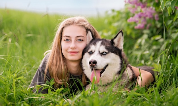 Siberian Husky i jego piękna niebieskooka właścicielka przytulają się leżąc na trawie Pojęcie miłości do zwierząt i natury