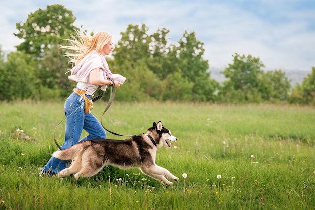 Siberian husky i jego właściciel biegają razem wesoło wzdłuż drogi na tle panoramicznego wiejskiego krajobrazu latem