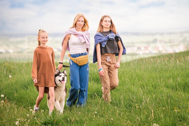 Siberian husky i rodzina jego właścicieli radośnie biegają razem wzdłuż drogi na tle panoramicznego widoku letniego wiejskiego krajobrazu