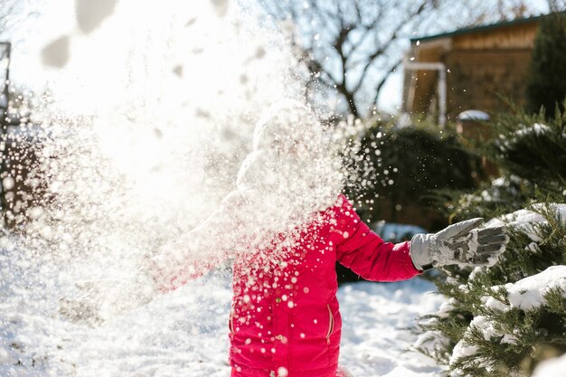 Siedmioletnia ładna Dziewczyna W Zimowe Ubrania Bawiące Się śniegiem Na Podwórku Domu W Słoneczny Zimowy Dzień.