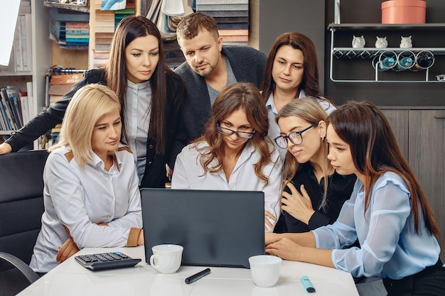 Siedmiu Odnoszących Sukcesy, Zapracowanych Pracowników Biurowych, Siedzących Przy Białym Stole I Patrzących Na Monitor Dziewczyny Piszącej Na Laptopie. Uważni Pracownicy. Proces Dyskusji. Koncepcja Wzrostu