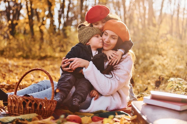 Zdjęcie siedząc na ziemi mama z małym synkiem i córeczką bawi się w jesiennym parku