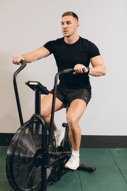 Siłacz używający roweru powietrznego do treningu cardio na siłowni cross trainingu