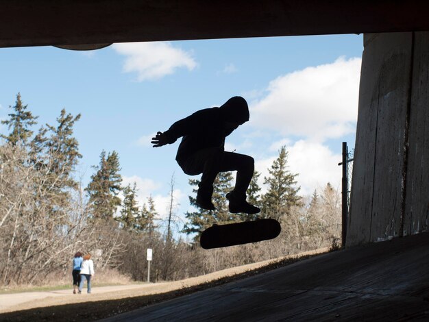 Zdjęcie silhoueta człowieka skaczącego ze skateboardem pod mostem