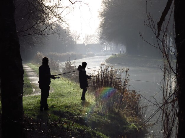 Zdjęcie silhoueta ludzi łowiących ryby, stojących na lądzie przy rzece przeciwko drzewom