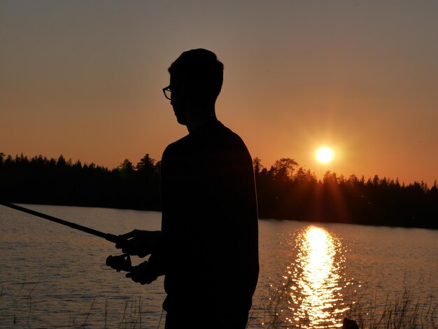 Zdjęcie silhueta mężczyzny łowiącej ryby w jeziorze na czyste niebo podczas zachodu słońca