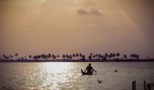Silhueta mężczyzny w łodzi na jeziorze na tle nieba podczas zachodu słońca