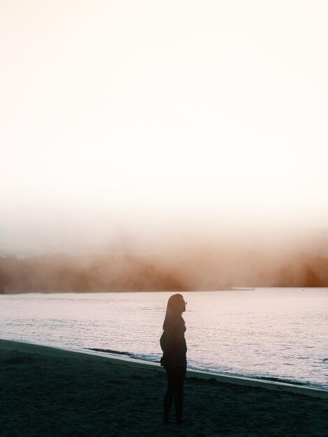 Silhueta młodej kobiety stojącej na plaży w mglistą pogodę