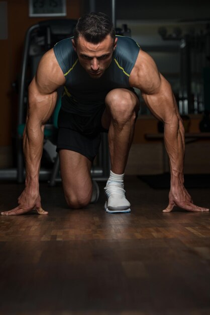 Silni muskularni mężczyźni klęczą na podłodze prawie jak sprinter w pozycji startowej