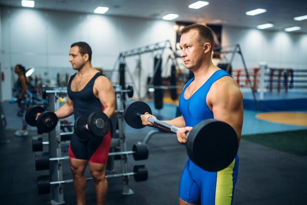 Silni sportowcy płci męskiej pracują z ciężarami na siłowni. Trening w podnoszeniu ciężarów w klubie sportowym lub fitness