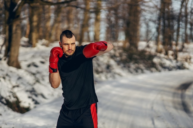 Silny bokser w rękawicach bokserskich stojący na łonie natury w śnieżny zimowy dzień i sparing. Boks w przyrodzie, zdrowe życie, sporty zimowe