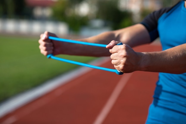 Silny fitness człowiek robi trening z gumką na świeżym powietrzu na stadionie. Miejsce na tekst