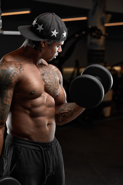 Silny i muskularny mężczyzna o ciemnej skórze trenuje na nowoczesnym sprzęcie w siłowni Portret mięśnia napompowanego trenera fitness