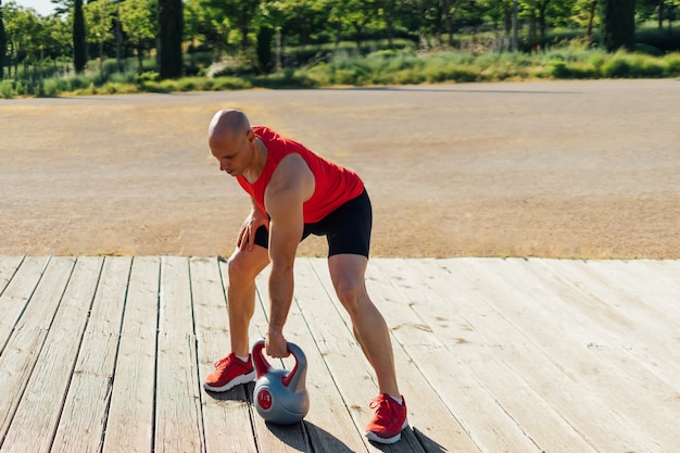 Zdjęcie siłownia mężczyzna robi trening kettlebell na drewnianej platformie.