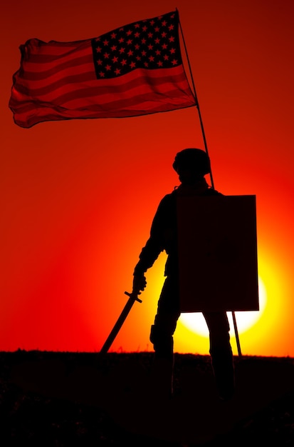 Silueta amerykańskiego żołnierza armii uzbrojonego w miecz i tarczę stojącego pod machającą amerykańską flagą narodową na tle zachodu słońca bohater armii i patriot wojskowy chwała i cześć pamięci poległych żołnierzy