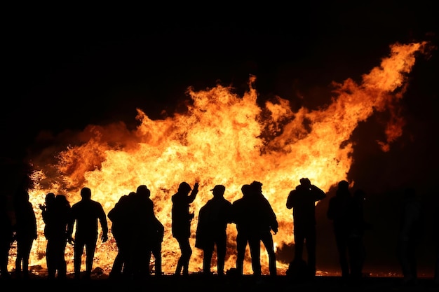 Siluweta ludzi stojących przy ogniu w nocy