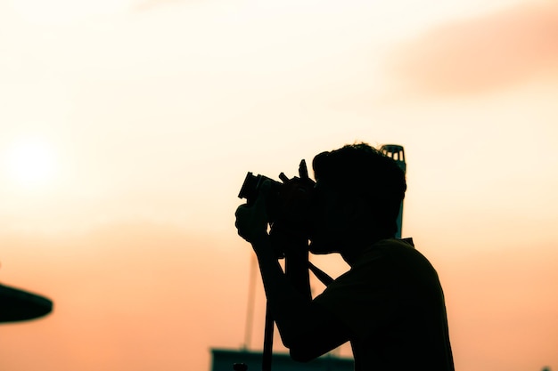 Siluweta osoby fotografującej na jasnym niebie