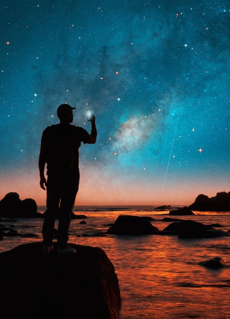 Siluweta osoby na skale robiącej zdjęcia komórką w nocy Drogi Mlecznej