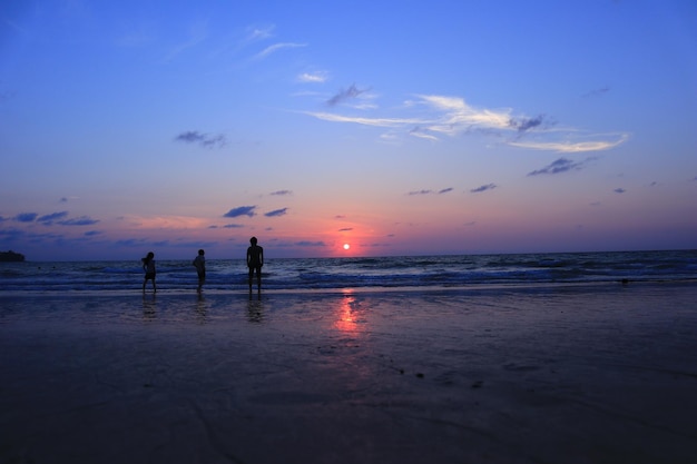 Siluwety ludzi na plaży na tle nieba podczas zachodu słońca