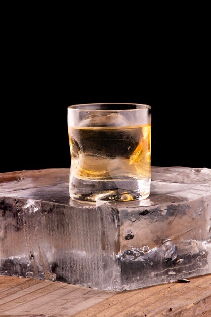 Zdjęcie single malt whisky na skałach z przezroczystym lodem w kulce izolowanej na drewnianym stole nad blokem lodu z przodu