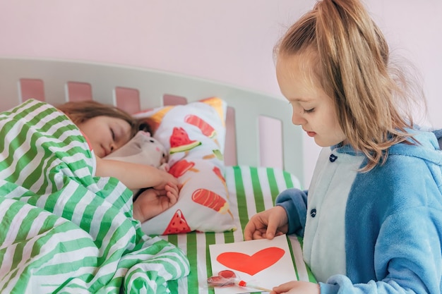 siostra daje swojej młodszej siostrze, która wciąż śpi w łóżku, ręcznie robioną kartkę