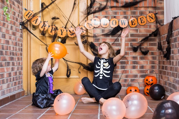 Zdjęcie siostry bawiące się balonami siedząc na podłodze w domu podczas halloween